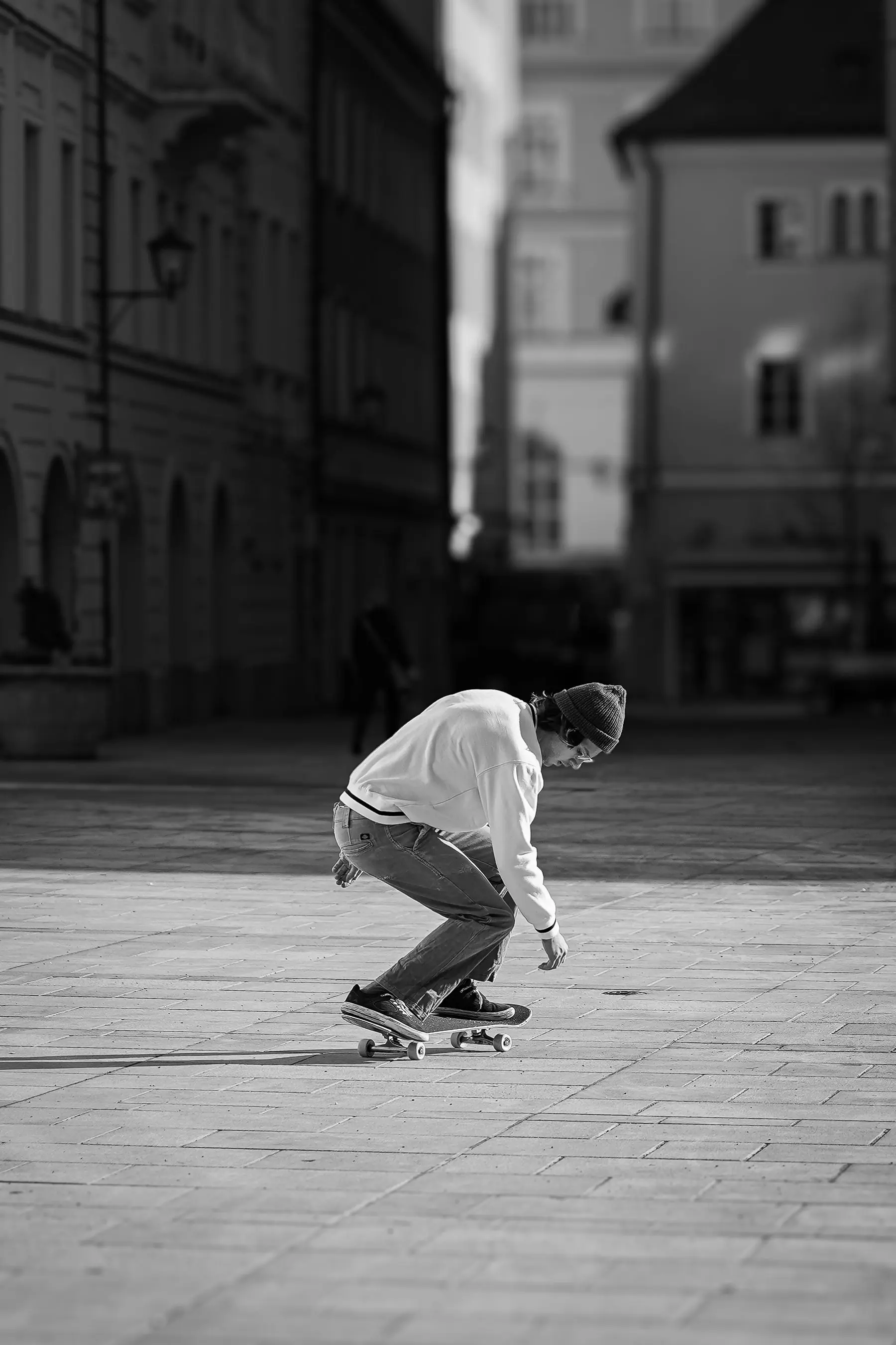 Skateboarder in a white sweater rolling through an empty plaza